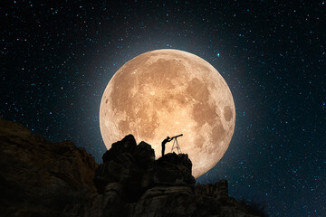 Fantasy landscape. The full moonrise over the rock. Man silhouette with telescope explore starry...