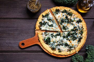 Healthy, low carb cauliflower crust pizza with kale and pesto sauce. Above view with cut slices....
