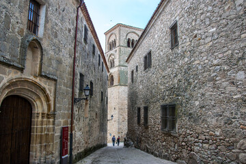 Dos casas palaciegas con fachadas de piedra convergen en una calle hacia la torre de una iglesia en la localidad española de Trujillo