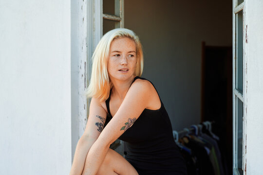 Relaxed young woman in bodysuit sitting on windowsill