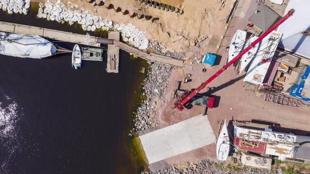 Time-lapse of the big industrial crane lifts the sailboat and floats it, the beginning of a season of sailing, a skyscraper on a background, drone view point
