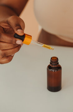 Crop hand of African woman holding pipette with skincare oil