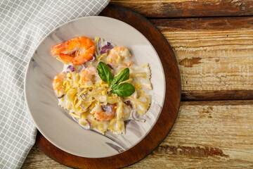 Farfalle pasta with shrimps in a creamy sauce on a gray plate on a wooden table on a light napkin.