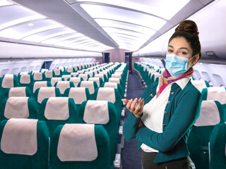 A beautiful flight attendant in a green jacket and mask in front of an airplane aisle. Subject on...
