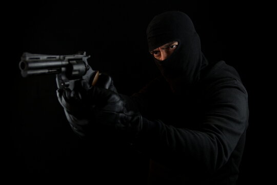 Man with black mask holding pistol, standing shooting with a gun, isolated on black background.