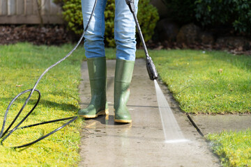 Woman power washing the garden back yard path using a high pressure hose with jet attachment