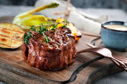 Grilled beef tenderloin steak on a wooden board with grilled vegetables. Filet Mignon recipe concept, selective focus