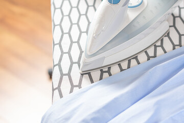 Electric iron and shirt on the ironing board in the room