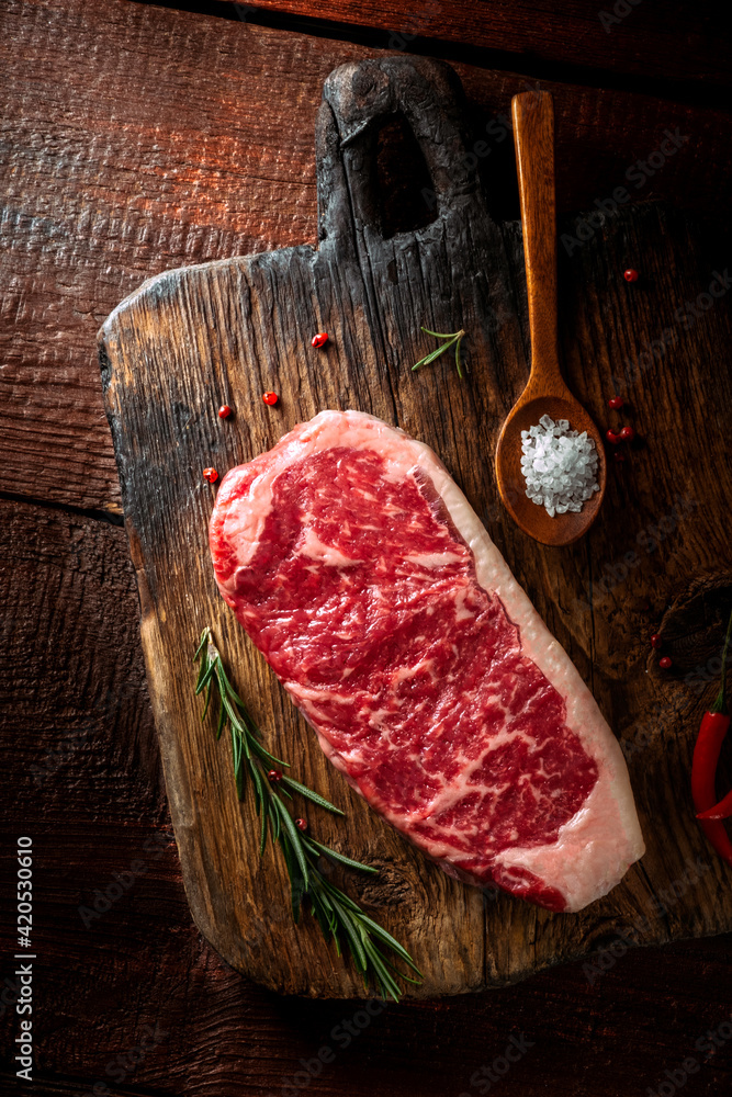 Wall mural Raw striploin steak (New York) of beef on a seasoning board. Rustic style with wooden old background, top view