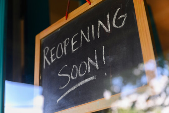 Reopening Soon"" sign hanging in small business window