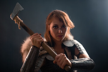 Portrait of a medieval, fantasy viking woman with an ax in her hands in the dark. Female warrior...