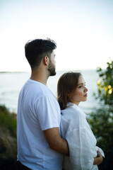 Obraz premium the guy from behind hugs the girl while standing on the slope of the lake of the sea and the river and look into the distance. romantic relationship. love story