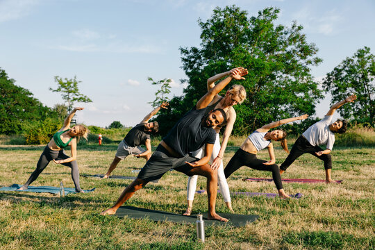 Female Yoga Teacher Helping Male Student During Outdoor Yoga Class