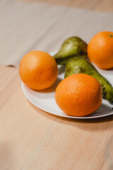 a white plate of fruit on the kitchen table, pears and oranges. still life. healthy snack. vitamins and fiber. farm products. ingredients for dessert or sweet drink