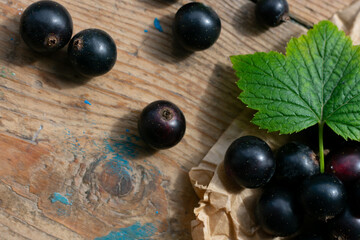 Group of ripe black currants on wooden table with green leaf, source of vitamin C, vegetarian food, berries