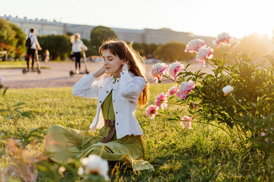Young female sitting on lawn with blooming peony in public place