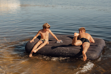 Two boys swim on an inflatable mattress