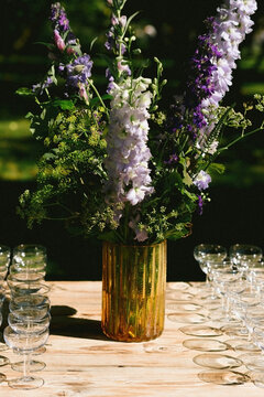 Yellow Vase With Green And Purple Flowers On A Wooden Table With Empty Champagne Glasses