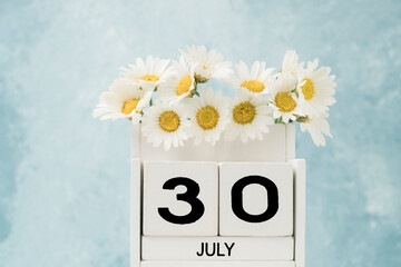 Cube calendar for july decorated with daisy flowers on blue with copy space
