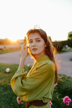 Portrait of young female standing on lawn with blooming peony in public place