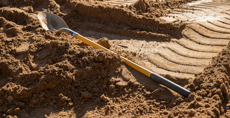Spade shovel tool with wooden handle for digging into the earth lays on the dirt at a house construction site.