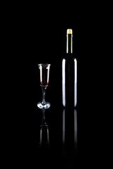Dark red wine bottle with cork and goblet with red wine on black reflective surface