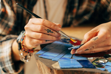 Women's hands collect colored pieces of smalt mosaic while putting the clue