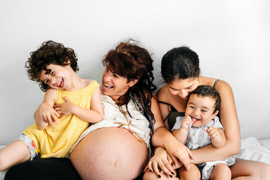 Multiethnic family with pregnant mother posing together on bed against white wall