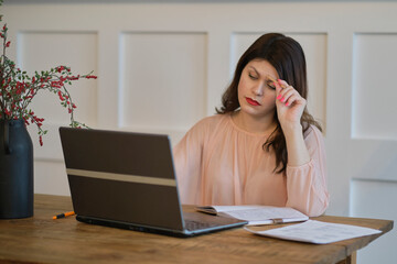 Portrait of a young tired businesswoman using laptop and working on some reports from home.
