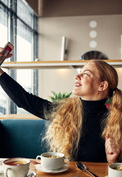 a girl with long blond curly hair takes a picture of herself on the phone in a cafe