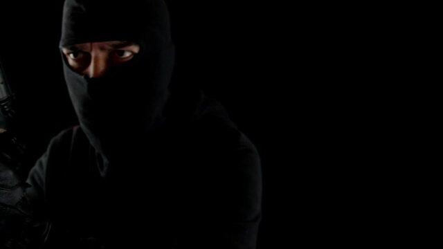Thief with balaclava and gun in the dark with threatening look.