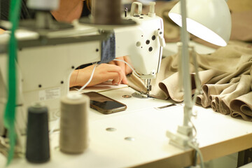 Female hands stitching white fabric on professional manufacturing machine at workplace. Close up view of sewing process. Light blurred background