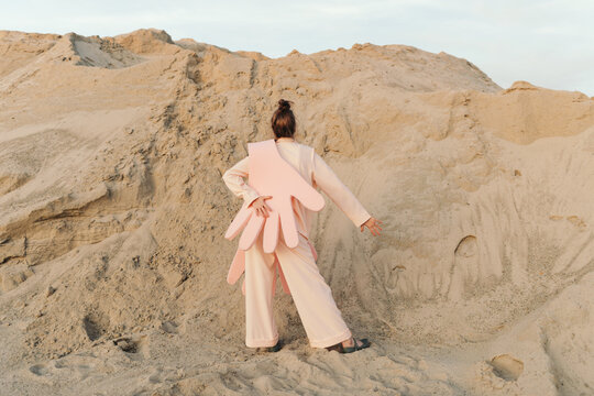 Unrecognizable female in pink pantsuit standing on sand