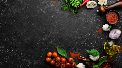Kitchen cooking background: cherry tomatoes, onions, spices and herbs. On a black background.