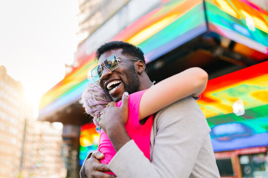 Smiling black man embracing unrecognizable beloved near colorful building