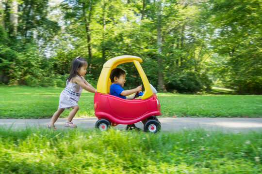 Asian siblings running with a toy car in the park