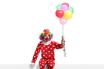 Clown sitting on a banner and holding a bunch of balloons