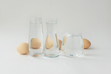 Image of eggs through distortion of water in three transparent vessels on white background, copyspace. Creative idea concept, unusual reflection of food ingredients.