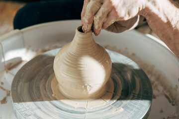 Professional potter working with clay on potter's wheel in workshop or studio