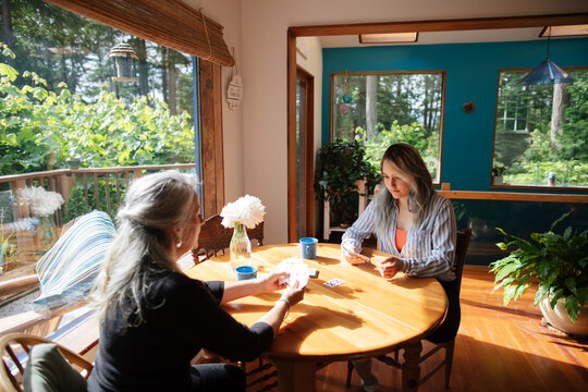 Mother and daughter playing cards on sunlight table.