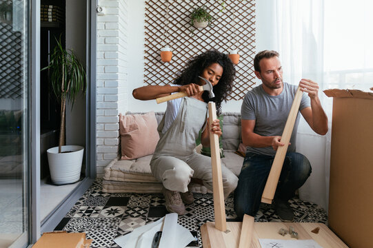 Multiracial couple installing wooden furniture together