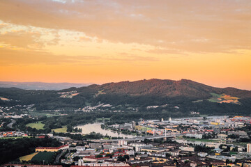 sunset falls on city of Linz in northern Austria. Beautiful orange sky and the eastern part of city. Linzertorte is immersed in red-orange light and sky is reflected from the Danube River