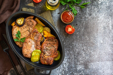 Summer Ketogenic diet lunch or dinner. Grilled pork loin on the bone with baked vegetables in a cast iron frying pan on a dark stone countertop. Top view flat lay. Copy space.