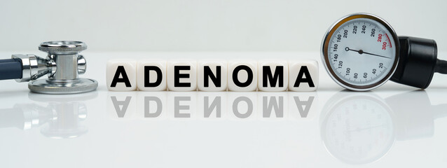 On a reflective white surface lies a stethoscope and cubes with the inscription - ADENOMA