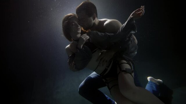 young loving pair is hugging underwater, man is stroking his beautiful girlfriend dressed lingerie