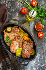 Summer Ketogenic diet lunch or dinner. Grilled pork loin on the bone with baked vegetables in a cast iron frying pan on a dark stone countertop. Top view flat lay. Copy space.