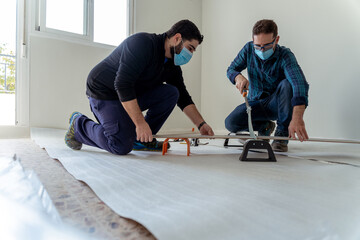 Two young men with mask cutting a wood laminate with a guillotine to install a wooden floor in their apartment - 420546005