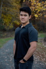 Outdoor lifestyle portrait of handsome young man wearing short sleeve black shirt looking at camera with path in background
