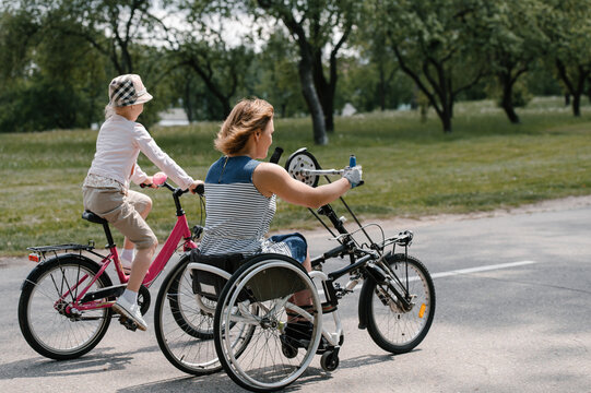 Unrecognizable mother with disability and daughter riding bikes through countryside