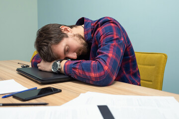 Young tired businessman sleeping at his desk in the office. Overwork, side view